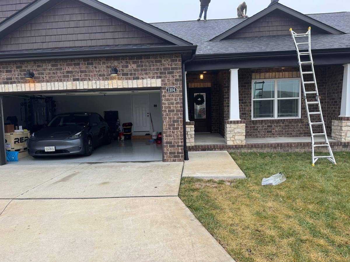 George's brick home — installer on roof, Tesla in garage